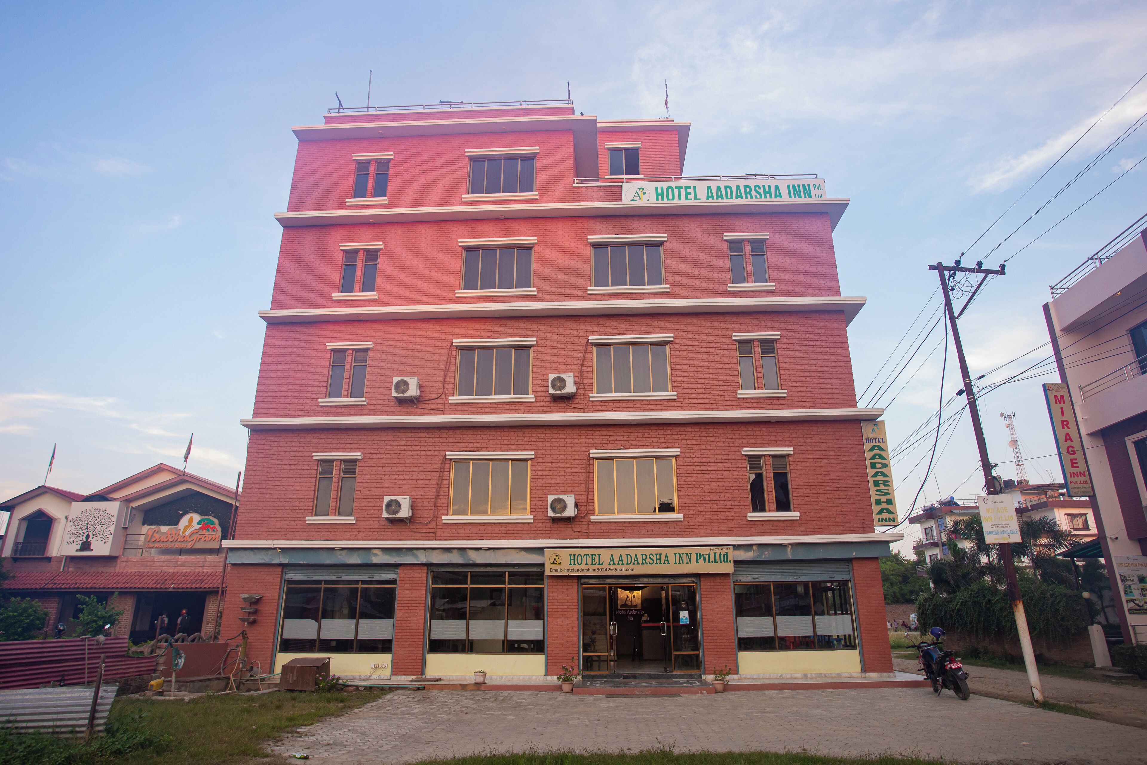 Un hôtel à plusieurs étages, doté d’une façade rouge, de grandes fenêtres et d’une enseigne indiquant qu’il s’agit de l’hôtel Aadarsha Inn.