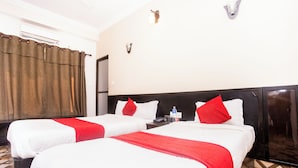 A hotel room with two beds, each with white bedding and red accents, a nightstand with a phone and a bottle, and a patterned floor.