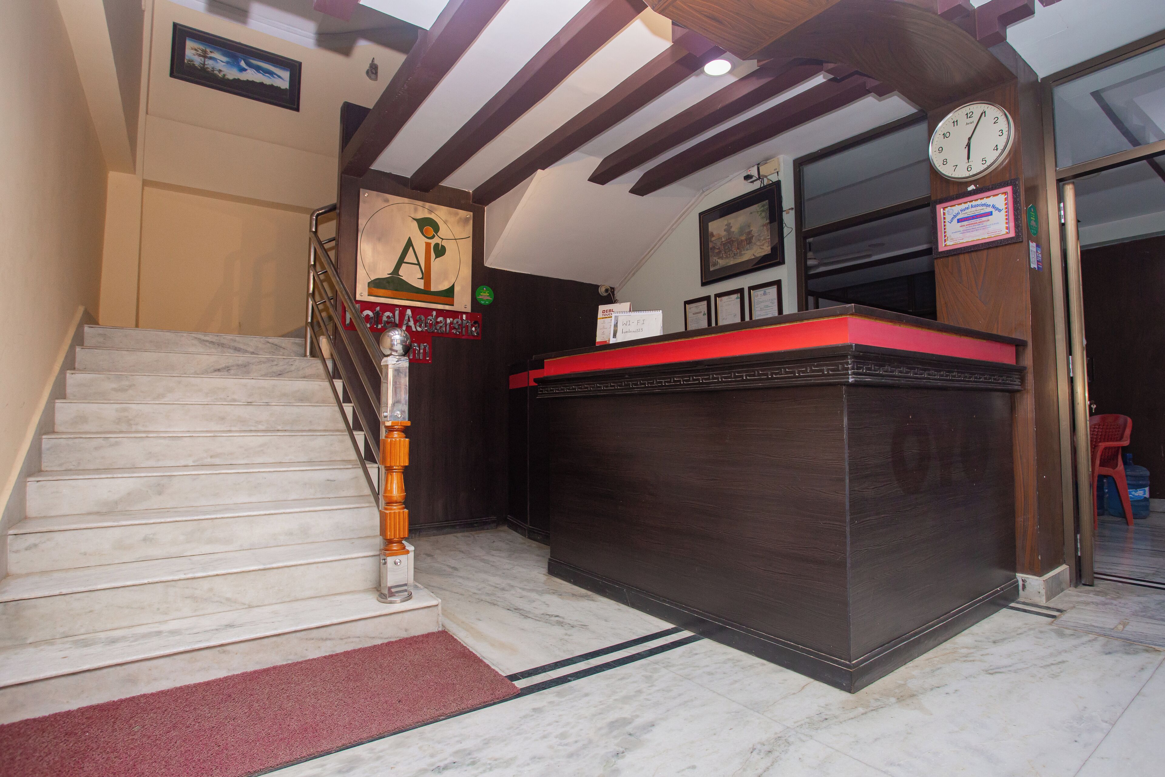 A hotel reception area with a marble staircase, a reception desk, and a clock on the wall.