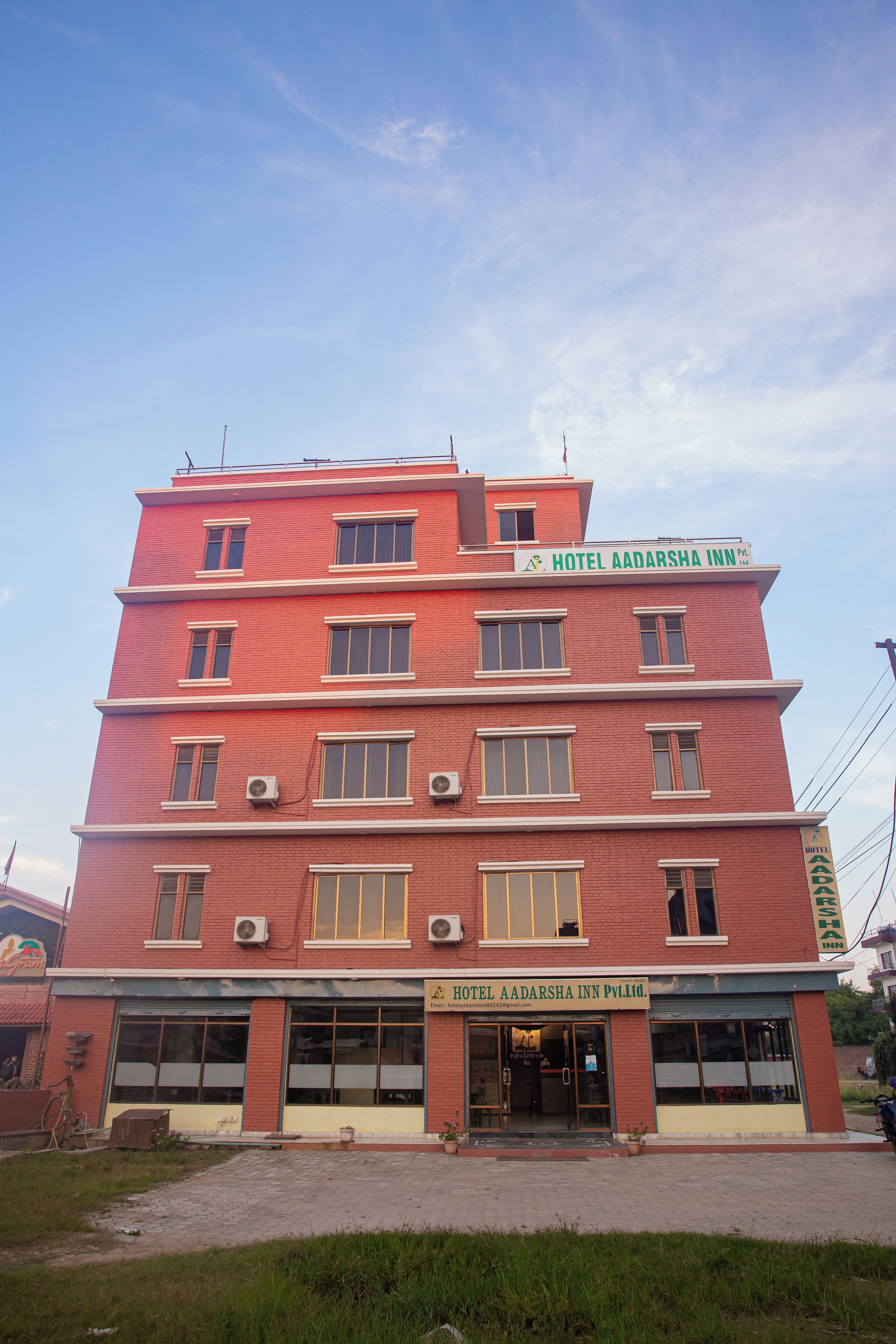 A multi-story hotel with a red facade, multiple windows, and a sign indicating it is Hotel Aadarsha Inn.