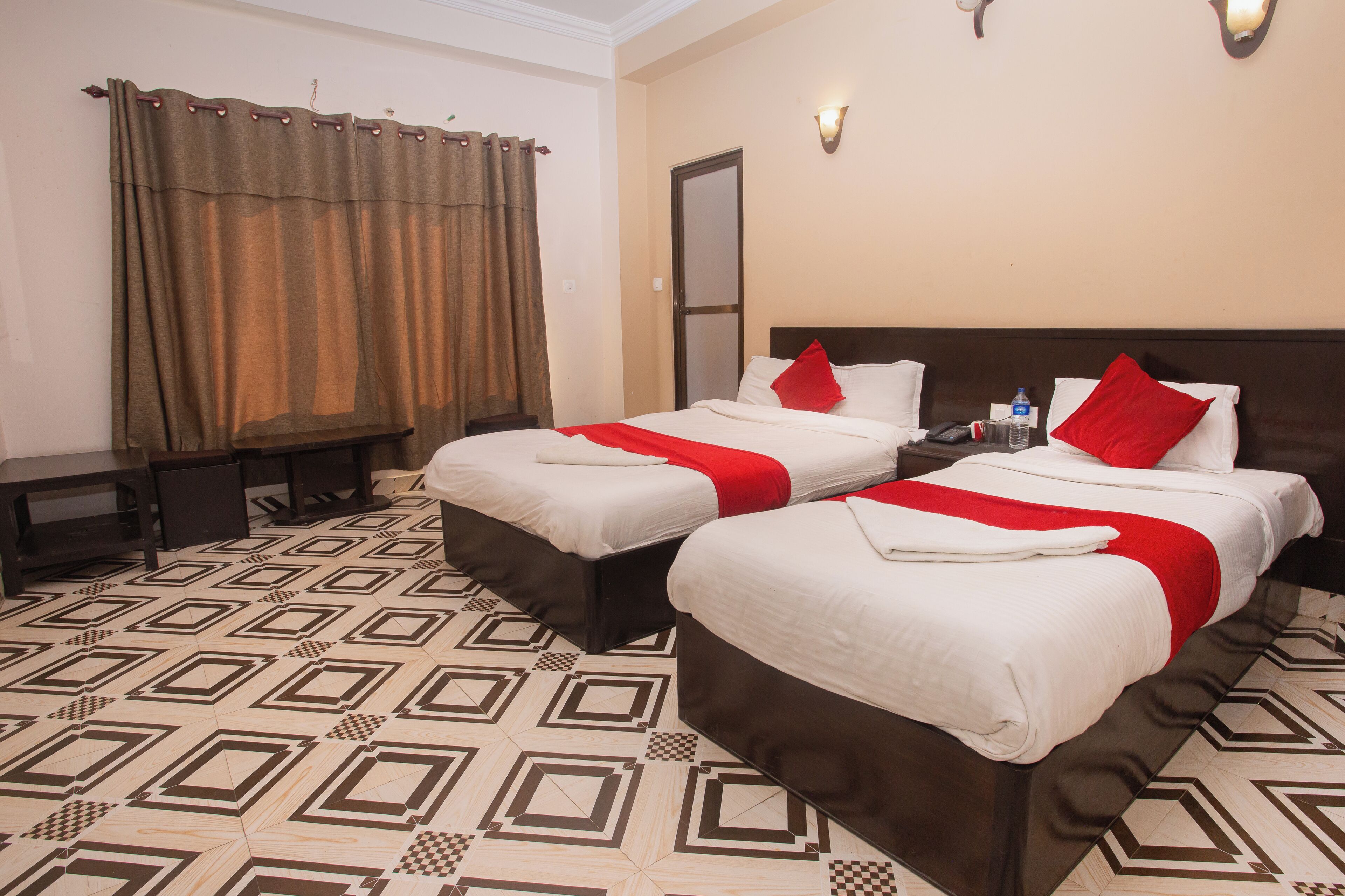 A hotel room with two beds, a checkered floor, a curtain, and a wall-mounted light fixture.