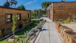 A wooden cabin with a patio area, a small garden, and a clear sky. - Villas P Moinho - 04 Macieira (Obidos)