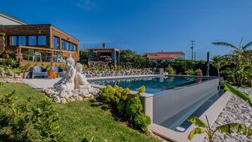 Un área de piscina moderna con una estatua de Buda, sillones de descanso y una terraza de madera.
