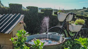A garden with a water fountain, a bicycle with baskets, and a wooden structure. - Villas P Moinho - 04 Macieira (Obidos)