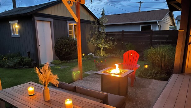 An outdoor patio area with a wooden table, two candles, a small fire feature, and a red chair.
