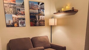 A cozy living room with a brown sofa, a wooden coffee table with a magazine, and a wall-mounted shelf with candles.
