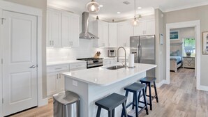 A modern kitchen with white cabinets, a central island with stools, stainless steel appliances, and pendant lighting. - Touchdown Hideaway! Beach/OWA/Sports/Shopping (Foley)