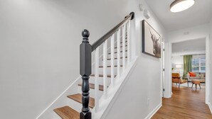 Un escalier avec des marches en bois et une balustrade noire, menant à une pièce où se trouvent un rideau vert et un canapé.