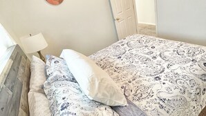 Een slaapkamer met een bed, kussens, een lamp en een deur.
