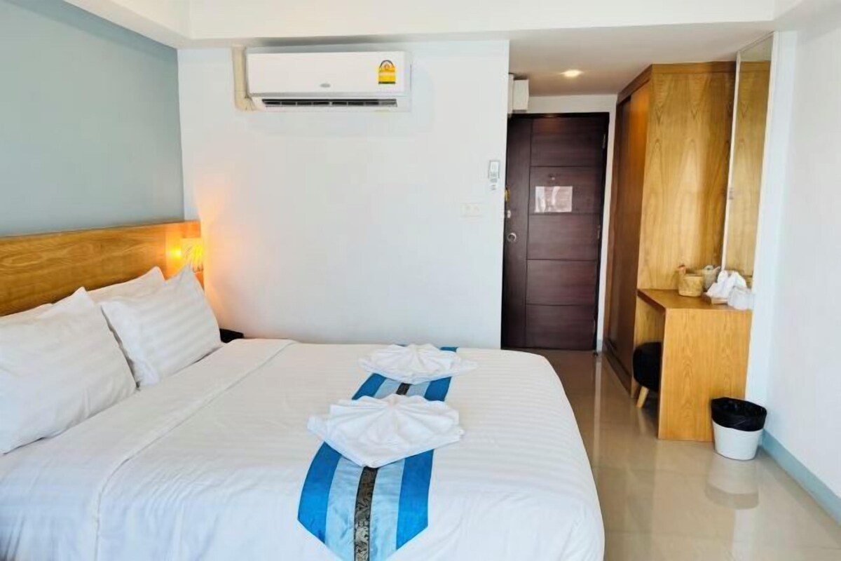 A hotel room with a bed, a desk, and an air conditioning unit.