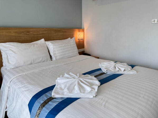 A neatly made bed with white linens and a blue and white striped blanket, a wooden headboard, and a wall-mounted light fixture. - Collection O Room Lanna Hotel (Chiang Mai)