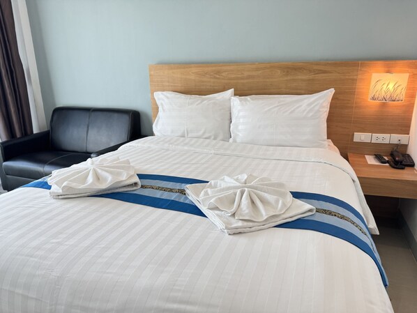 A neatly made bed with white and blue striped bedding, a wooden headboard, and a bedside table with a phone and a lamp.