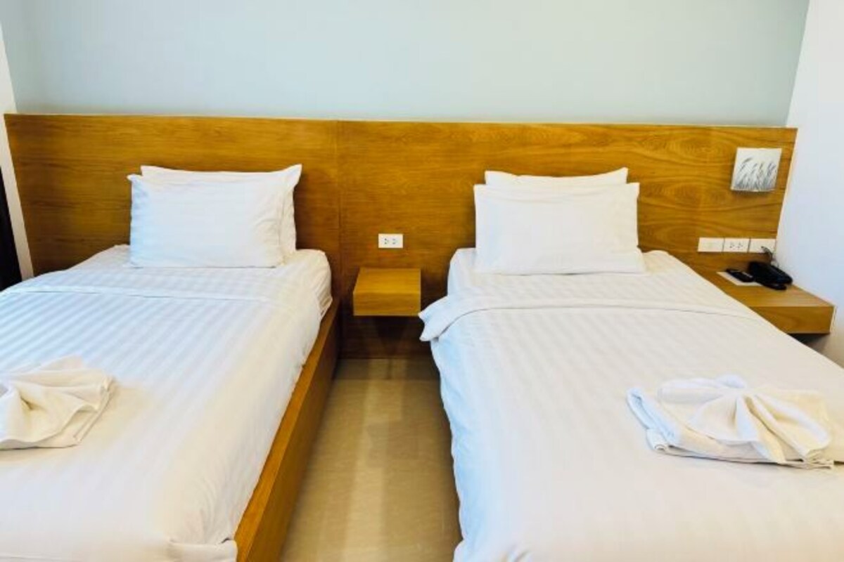 Two single beds with wooden headboards, white linens, and bedside tables with lamps and phones.
