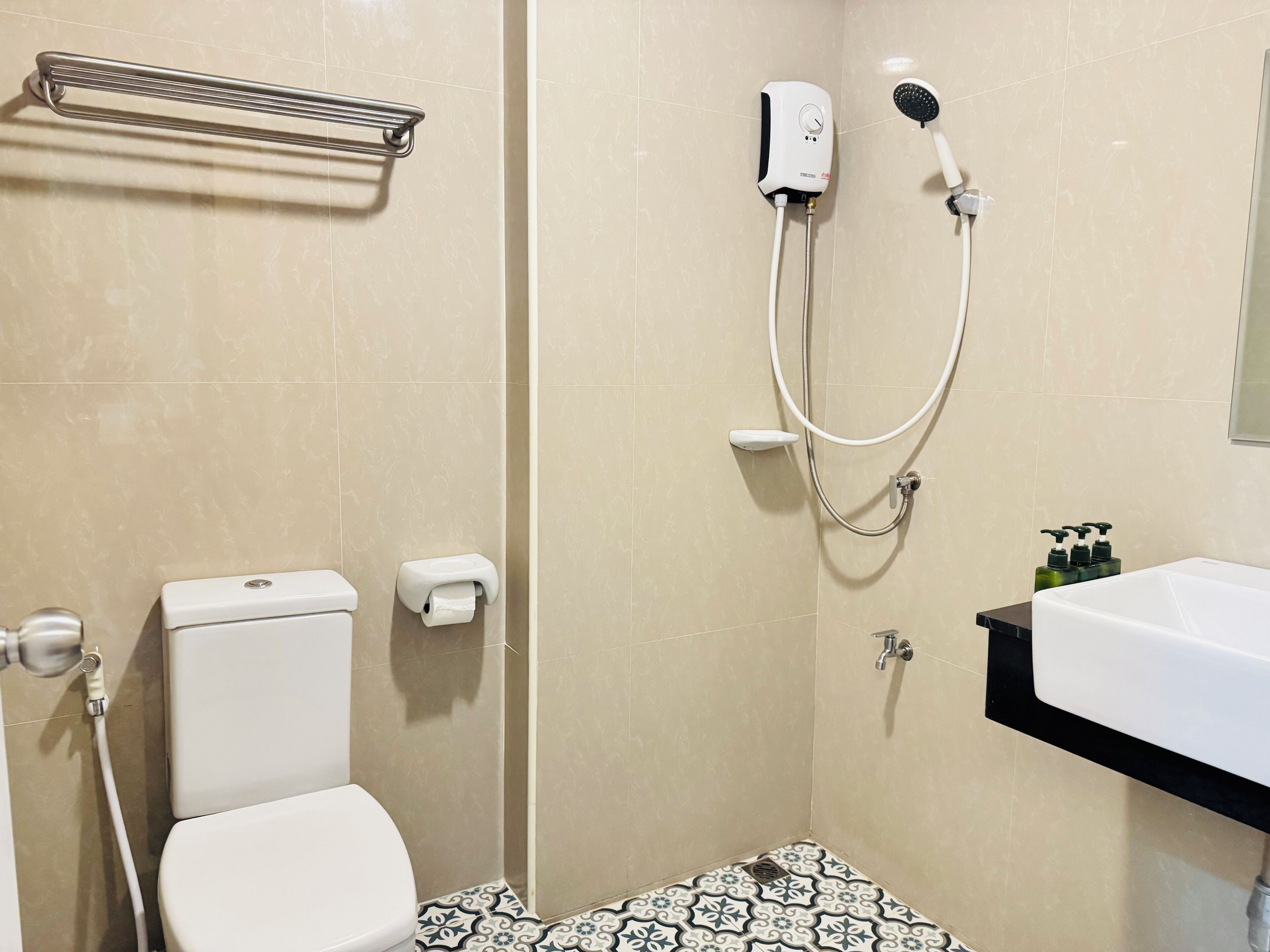 A bathroom with a toilet, a shower with a handheld showerhead, a toilet paper holder, and a sink with soap dispensers.