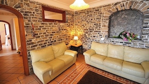 Ein gemütliches Wohnzimmer mit Steinwänden, zwei sofas in Cremefarben, einem kleinen Tisch mit einer Lampe und einem Kamin mit Blumen.