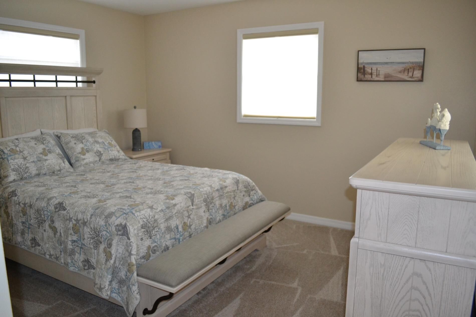 Une chambre à coucher avec un lit, une table de chevet, une lampe, une commode et un tableau au mur.