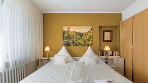 A hotel room with a large bed, two bedside tables with lamps, a painting on the wall, and a wardrobe.