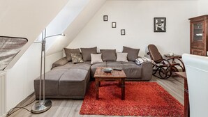 A modern loft bedroom with a sectional sofa, a wooden coffee table, a rocking chair, and a red rug.