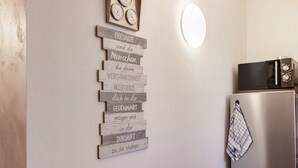 A kitchen with a wooden sign with text, a clock, and a microwave.