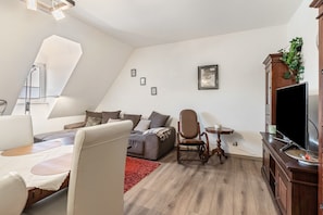 Ein modernes Wohnzimmer mit einer Couch, einem Sessel, einem kleinen Tisch und einem Fernseher.