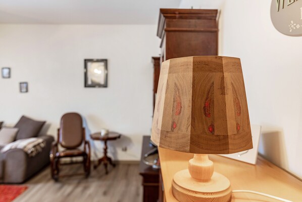 Une lampe en bois sur un bureau dans un salon, avec un canapé, un fauteuil et une horloge au mur.