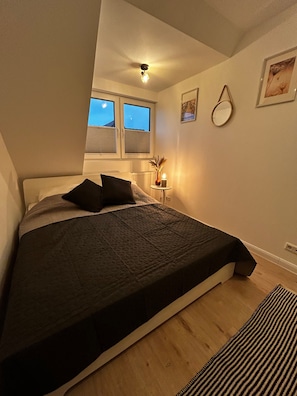 Une chambre à coucher avec un lit, une fenêtre, une table de chevet avec une lampe et une horloge murale.
