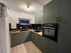 Une cuisine moderne avec des meubles gris, un plan de travail noir, un four encastré et une fenêtre au-dessus de l’évier.