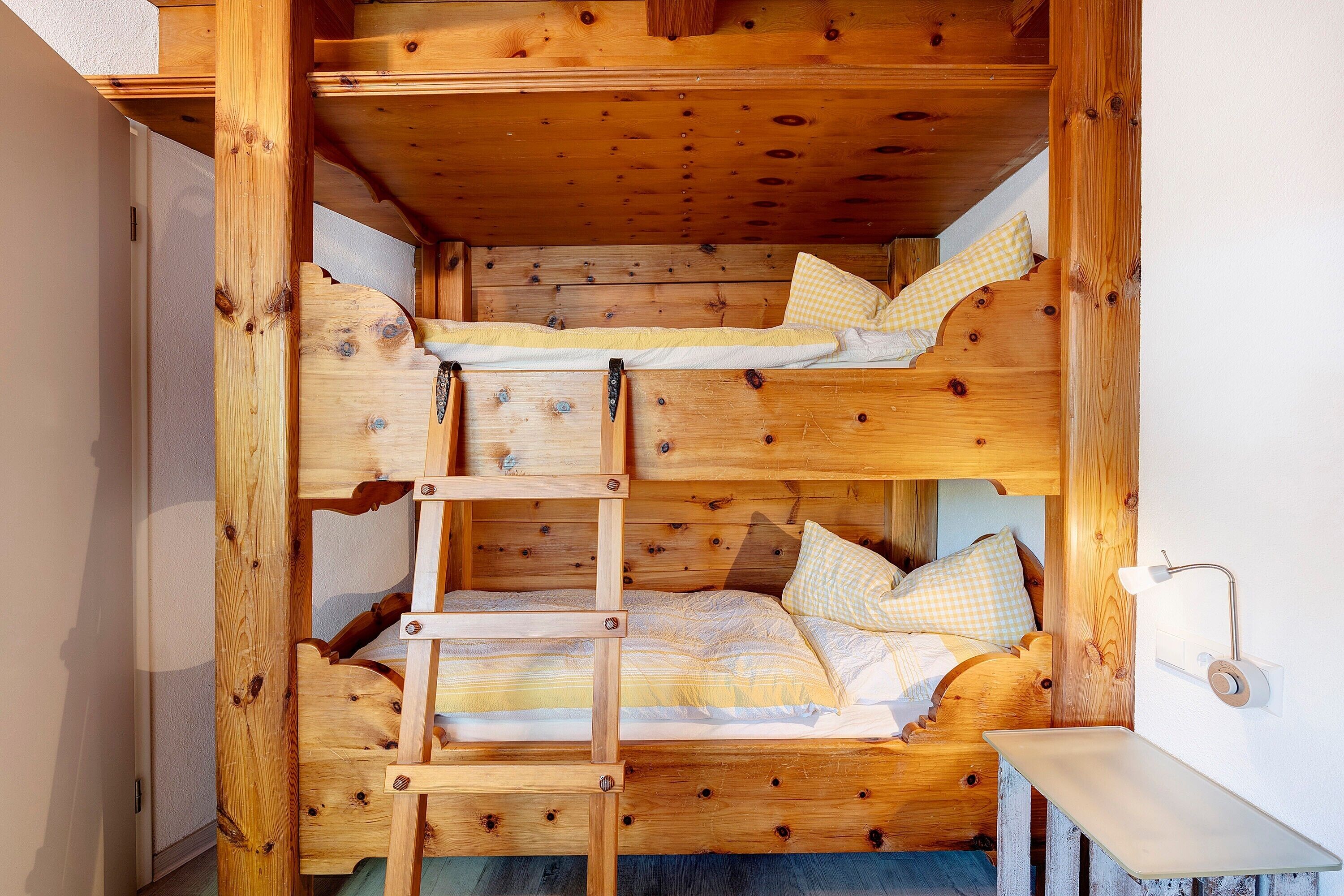 A bunk bed room with a ladder, wooden walls, and a small bedside table.