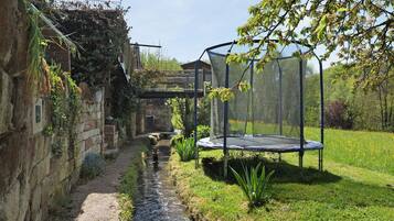 Een smalle watergang, een grasveld, een trampoline en een stenen muur.