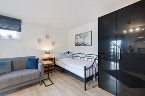 A compact room with a bed, a sofa, a bedside table, a lamp, and a wall-mounted artwork. - Apartment Knodel No. 3 in Kraichgau – Terrace, Garden & Wi-Fi (Sachsenheim)