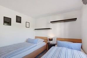 Ein Hotelzimmer mit zwei Einzelbetten, einem Nachttisch mit Lampe und einem Regal über den Betten.