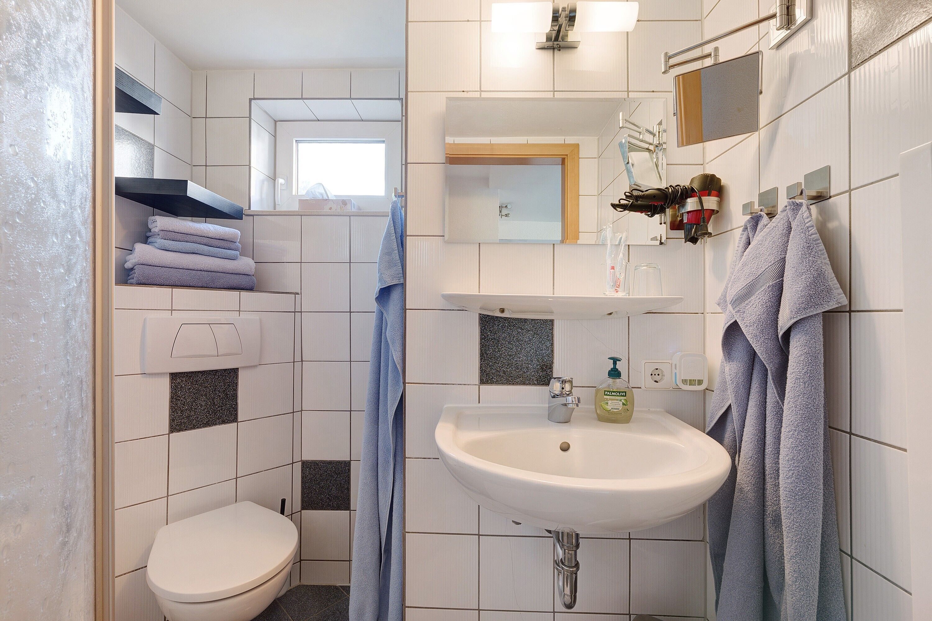 Un baño con inodoro, lavamanos, toallero y espejo.