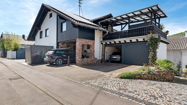 A two-story house with a garage, a covered balcony, and a stone wall. - Apartment Knodel No. 3 in Kraichgau – Quiet, Wi-Fi & Ideal for Business (Sachsenheim)