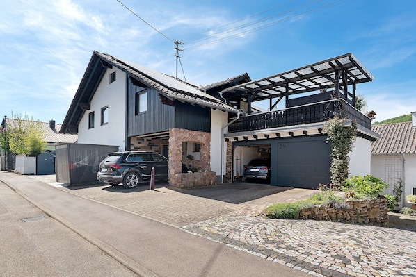 A two-story house with a garage, a covered balcony, and a stone wall. - Apartment Knodel No. 3 in Kraichgau – Terrace, Garden & Wi-Fi (Sachsenheim)