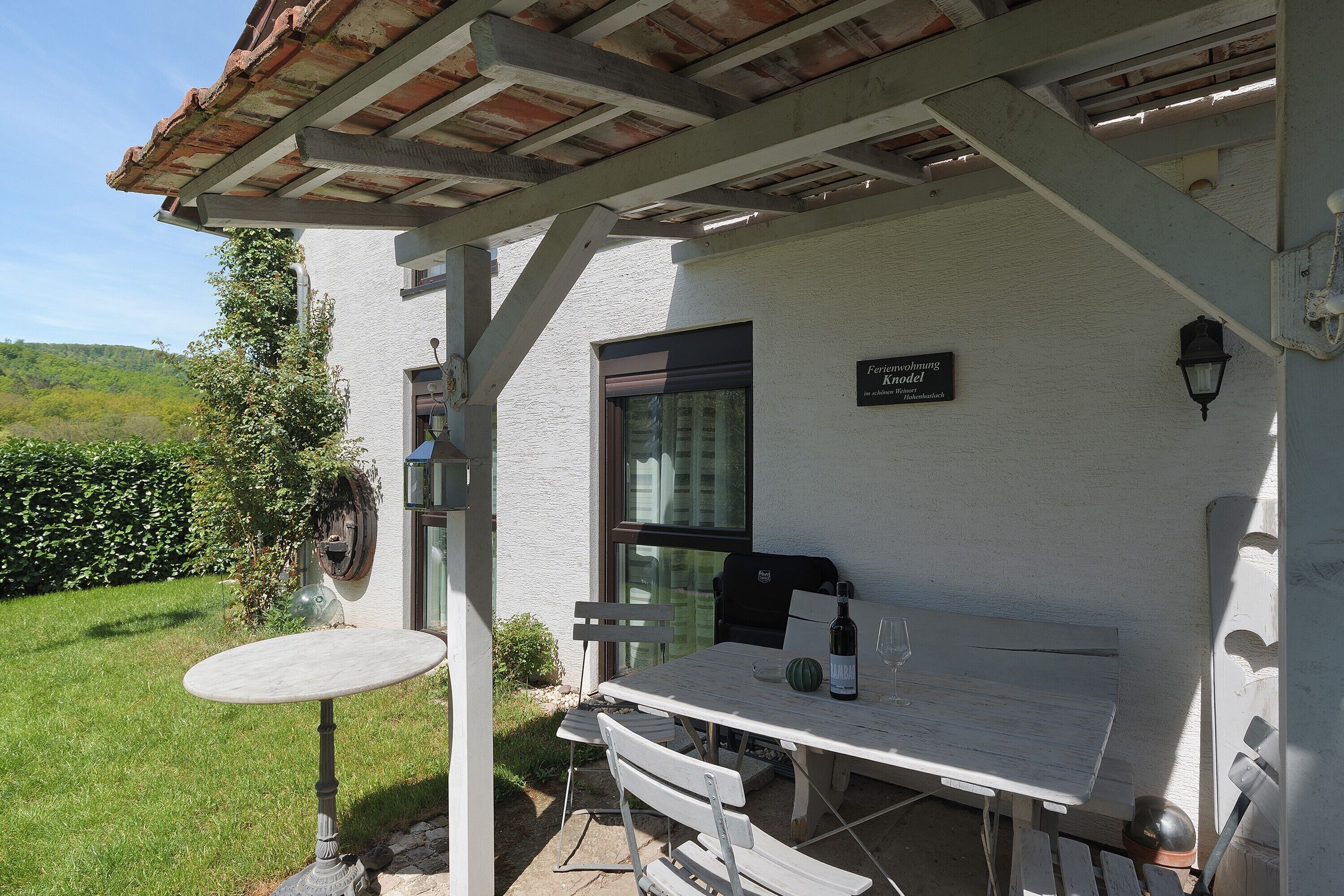 A patio with a table and chairs, a small garden, and a building with a sign.