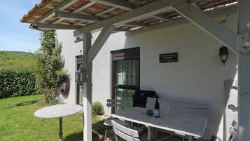 A patio with a table and chairs, a small garden, and a building with a sign.