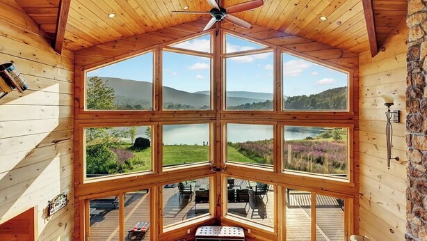 A cabin with a large central window and multiple smaller windows, offering panoramic views of a lake and surrounding landscape. - The Hunter Chalet (Hunter)