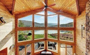 A cabin with a large central window and multiple smaller windows, offering panoramic views of a lake and surrounding landscape. - The Hunter Chalet (Hunter)