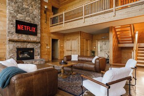 Un vaste espace de vie agrémenté d’une cheminée en pierre, de canapés en cuir, d’une table basse et d’un panneau indiquant la présence de Netflix.