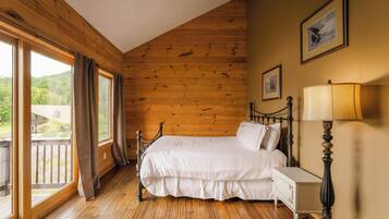 Une chambre avec un plancher en bois, un lit avec une literie blanche, une table de chevet, une lampe et une fenêtre avec des rideaux.