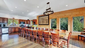 A spacious kitchen with wooden cabinets, a dining area with wooden chairs, and large windows offering a view of the outdoors. - The Hunter Chalet (Hunter)