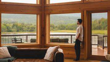 A spacious room with large windows, a wooden floor, a brown leather sofa, and a wooden coffee table.