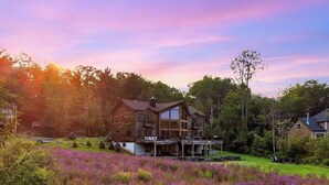 A large log cabin with a glass extension, surrounded by a lush garden and purple flowers. - The Hunter Chalet (Hunter)