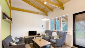 A modern living room with a wooden ceiling, a sofa, a chair, a coffee table, and a TV. - Apartment 'Fewo Am Flämingrand' with Shared Garden, Balcony and Wi-Fi (Zahna-Elster)