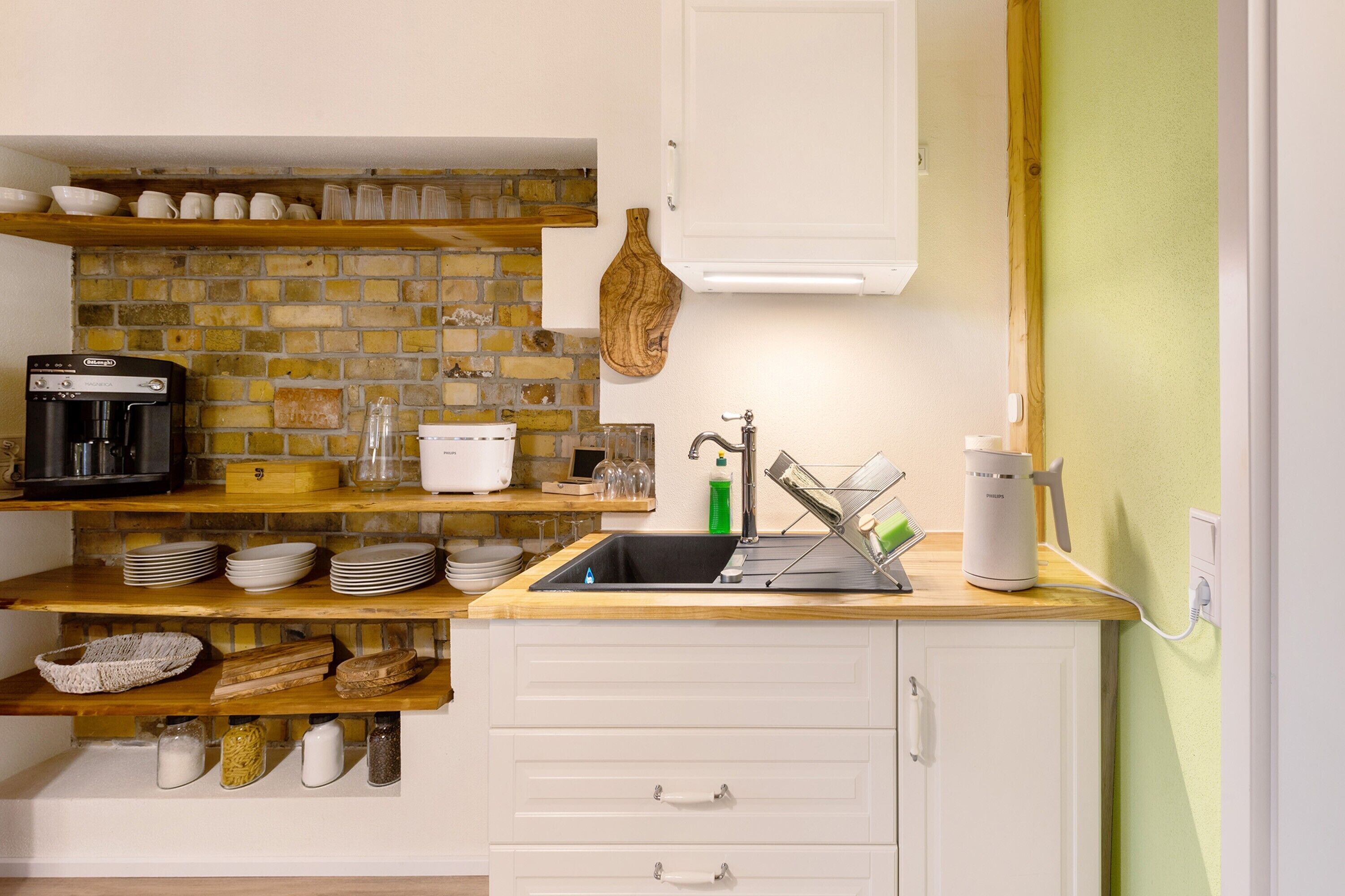 A kitchen with a brick backsplash, white cabinetry, a coffee machine, and a sink.