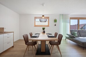 Ein Essbereich mit Holztisch, Stühlen, einer Chandelierleuchtre und Blick ins Freie.