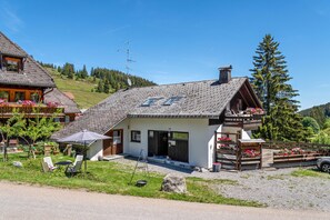 A chalet-style building with a sloped roof, a wooden balcony, and a gravel driveway.