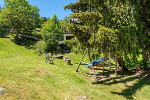A grassy outdoor area with a swing set and a slide, surrounded by trees and a building in the background. - Apartment 'Fingerhut' with Mountain View, Private Terrace and Wi-Fi (Feldberg (Schwarzwald))