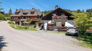 A traditional chalet-style building with a gravel driveway, a parked car, and a sign indicating a restaurant. - Apartment 'Fingerhut' with Mountain View, Private Terrace and Wi-Fi (Feldberg (Schwarzwald))