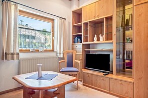 A room with a window, a table with a vase, a chair, a television, and wooden shelves with various items. - Apartment 'Fingerhut' with Mountain View, Private Terrace and Wi-Fi (Feldberg (Schwarzwald))